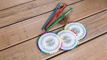 Set of colorful crochet hooks and several wheels of sewing pins arranged neatly on a wooden surface. photo