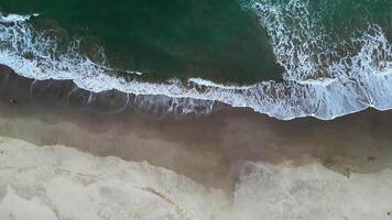 An artistic aerial view shows large waves crashing against a sandy beach, creating interesting patterns on Sawarna Beach, Banten, Indonesia. video