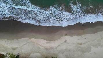 Aerial view tracking right, shows large waves crashing against a sandy beach, creating interesting patterns on Sawarna Beach, Banten, Indonesia. video