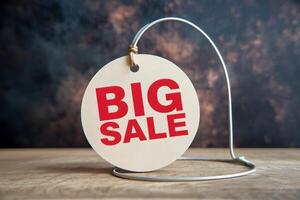 Circular tag reading BIG SALE hangs on wire against dark backdrop photo