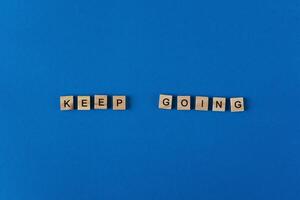 The phrase keep going is lined with wooden letters on a blue background top view. Postcard in place for text. Flatlay. The words. photo