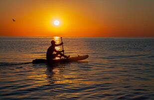 Silhouette of a man floating on a board with an oar. Dawn sun on the sea. Swimming on a supboard. Water active sports. Beautiful landscape. Sunset on the sea. Ocean coast. Copy space. photo