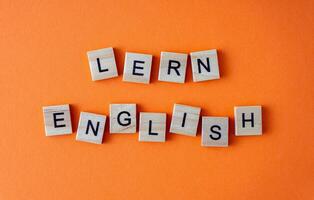 Word learn English. Motivation. The phrase is laid out in wooden letters top view. Motivation. Orange flat lay background. photo