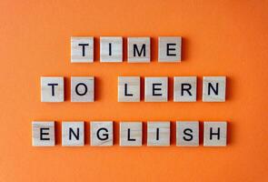 Word time to learn English. Motivation. The phrase is laid out in wooden letters top view. Motivation. Orange flat lay background. photo
