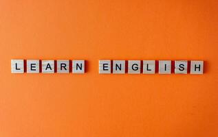Word learn English. Motivation. The phrase is laid out in wooden letters top view. Motivation. Orange flat lay background. photo