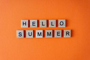 Hello summer word. The phrase is laid out in wooden letters top view. Motivation. Orange flat lay background. photo