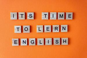 Word It is time to learn English. Motivation. The phrase is laid out in wooden letters top view. Motivation. Orange flat lay background. photo