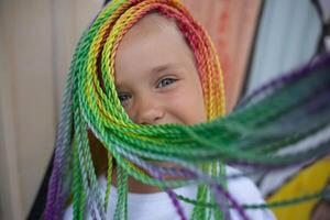 portrait of a little beautiful girl with multi-colored african braids on the background of a colorful wall photo