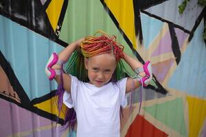 portrait of a little beautiful girl with multi-colored african braids on the background of a colorful wall photo