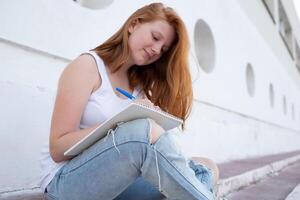 teenage girl draws in the sketchbook while sitting on the steps photo