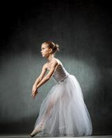 Beautiful young ballerina is dancing in the studio on a dark background. A little dancer. Ballet dancer. photo