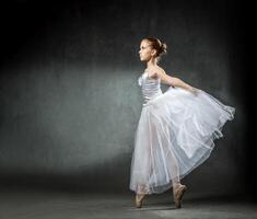 Beautiful young ballerina is dancing in the studio on a dark background. A little dancer. Ballet dancer. photo