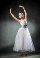 Beautiful young ballerina is dancing in the studio on a dark background. A little dancer. Ballet dancer. photo