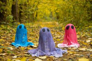 Halloween holiday concept. Handmade colorful ghosts made from bandages and glue in autumn forest background. Children's art project. DIY concept. photo