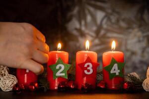 Four Advent red candles with numbers burning, fir branches and Christmas zero waste decorations in dark room in evening. Holiday preparation copy space for text. Catholic traditions of Christmas new year winter holidays photo