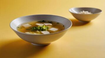 A bowl of miso soup with tofu and parsley on a yellow background photo