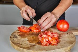 Close-up of hands using a knife to slice fresh tomatoes on a wooden cutting board in a kitchen setting. photo