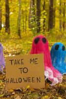 Halloween holiday concept. Handmade colorful ghosts with cardboard HAPPY HALLOWEEN message made from bandages and glue in autumn forest background. Children's art project. DIY concept. photo