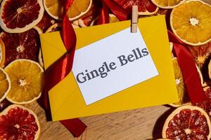 Christmas handmade wreath made of dried slices of orange and grapefruit with yellow envelope and paper note with GINGLE BELLS text. Winter holiday celebration greeting card. top view photo