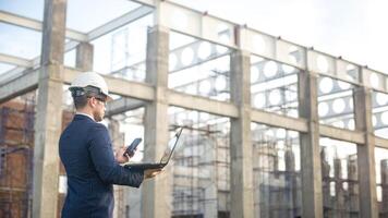 an architect engineer inspecting the building construction and check the progress of the construction plan on laptop, the foreman inspecting the building construction photo