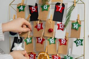 Number on craft paper notes with tasks before Christmas holidays. Female making kraft paper for handmade advent calendar Made with your own hands step by step DIY crafts do it yourself photo