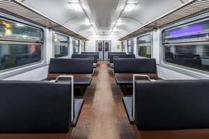 interior of an cheap empty train car with simple bench-style seating. The car features metal luggage racks above the windows, a clean, minimalist design, and a bright, neutral color scheme. photo