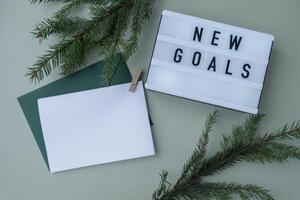 NEW GOALS text on Lightbox on green background with Christmas decor and copy space template mock up white envelope. New year aims resolutions. Planning and setting goals concept photo