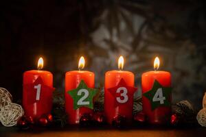 New year and Christmas preparation. Four red advent candles with numbers burning in dark background. Handmade eco-friendly decor. Sustainable Christmas decoration. Copy space photo