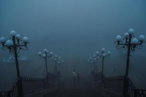 backs of a woman with a child boy going down the stairs on a foggy bridge in the city on an autumn morning in fog mist photo