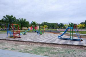 a playground in the park consisting of slides, seesaws, and hanging chairs. photo