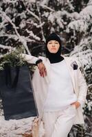 A girl in a white suit and balaclava with a package of Christmas trees in the winter forest on New Year's Eve.New Year's concept photo