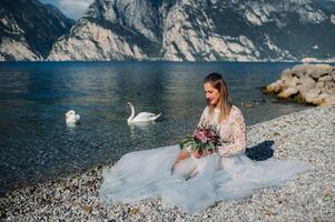 a girl in a smart white dress is sitting on the embankment of lake Garda.A woman is photographed against the background of a mountain and lake in Italy.Torbole photo