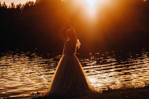 An elegant bride in a white dress enjoys nature at sunset.Model in a wedding dress in nature in the Park.Belarus photo