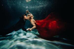 A woman in a red dress and a man in a suit are kissing underwater.A pair of floats under water photo