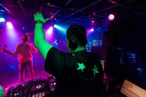 back of a male DJ with a raised hand in headphones at an electronic concert photo