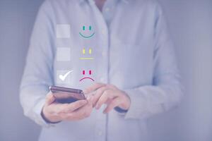 Businesswoman give sad face emoticon on virtual touch screen at smartphone. Concept customer service evaluation, satisfaction survey, questionnaire, feedback. User give rating to service experience. photo