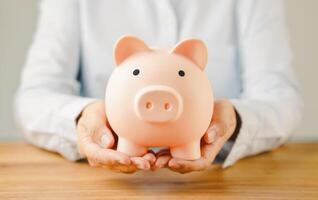Hand holding piggy bank on wood table. Save money for wealth, financial investment business, future education concept with copy space for input text. photo