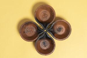 Close-up view of four traditional mud diyas arranged in floral pattern on yellow background photo