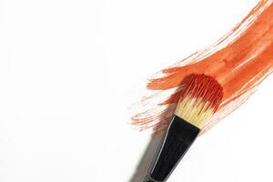 Red paint stroke on a white background with a brush to paint over it photo