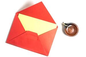 Red envelope with blank yellow paper greeting card with handmade clay diya isolated on white background for Diwali festival. photo