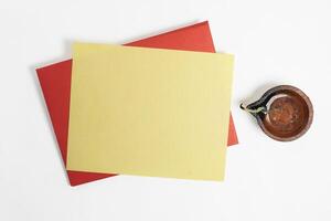 Handmade clay diya lamp with blank red and yellow paper greeting card envelope for Diwali festival on white background. Top view photo