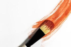 Vibrant red paint stroke on a white background with a brush to paint over it photo