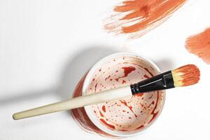 Paint brush on top of paint can with red paint on white background. photo