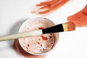 Paint brush on top of paint can with red paint on white background. Top view photo