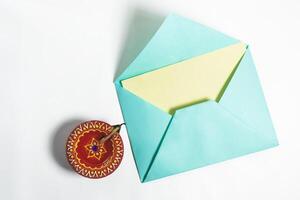 Vibrant envelope with blank note for festive greetings beside it traditional clay oil lamp on white background. photo