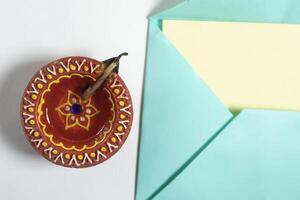 Happy Diwali greetings - colorful envelope with blank note for festive greetings card beside it traditional clay oil lamp on white background. photo