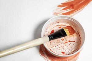 Paint brush on top of paint can with red paint on white background. Top view photo