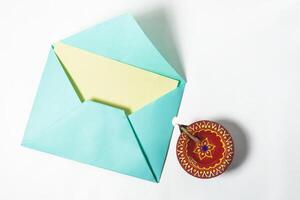 Top view of illuminated Diwali diya with open greeting card envelope on white background. photo
