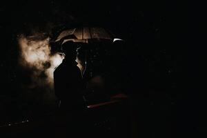 silhouette in the noir style of a male mafia detective in a raincoat and hat under an umbrella photo