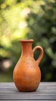 A traditional terracotta pitcher sits on a wooden table with a blurred green background. photo